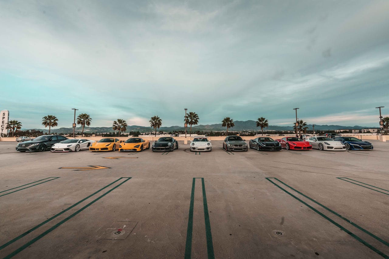 Lineup of luxury sports cars parked outdoors under a cloudy sky with palm trees.